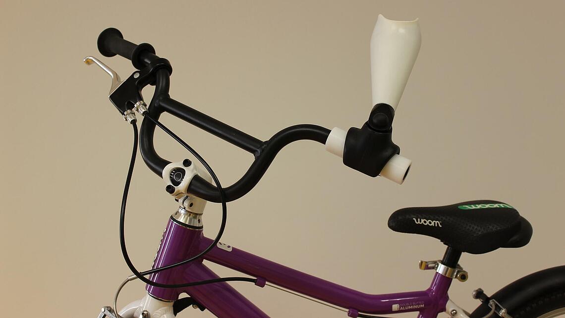 Unterarmprothese mit Adapter für einen Fahrradlenker an einem lila Kinderfahrrad