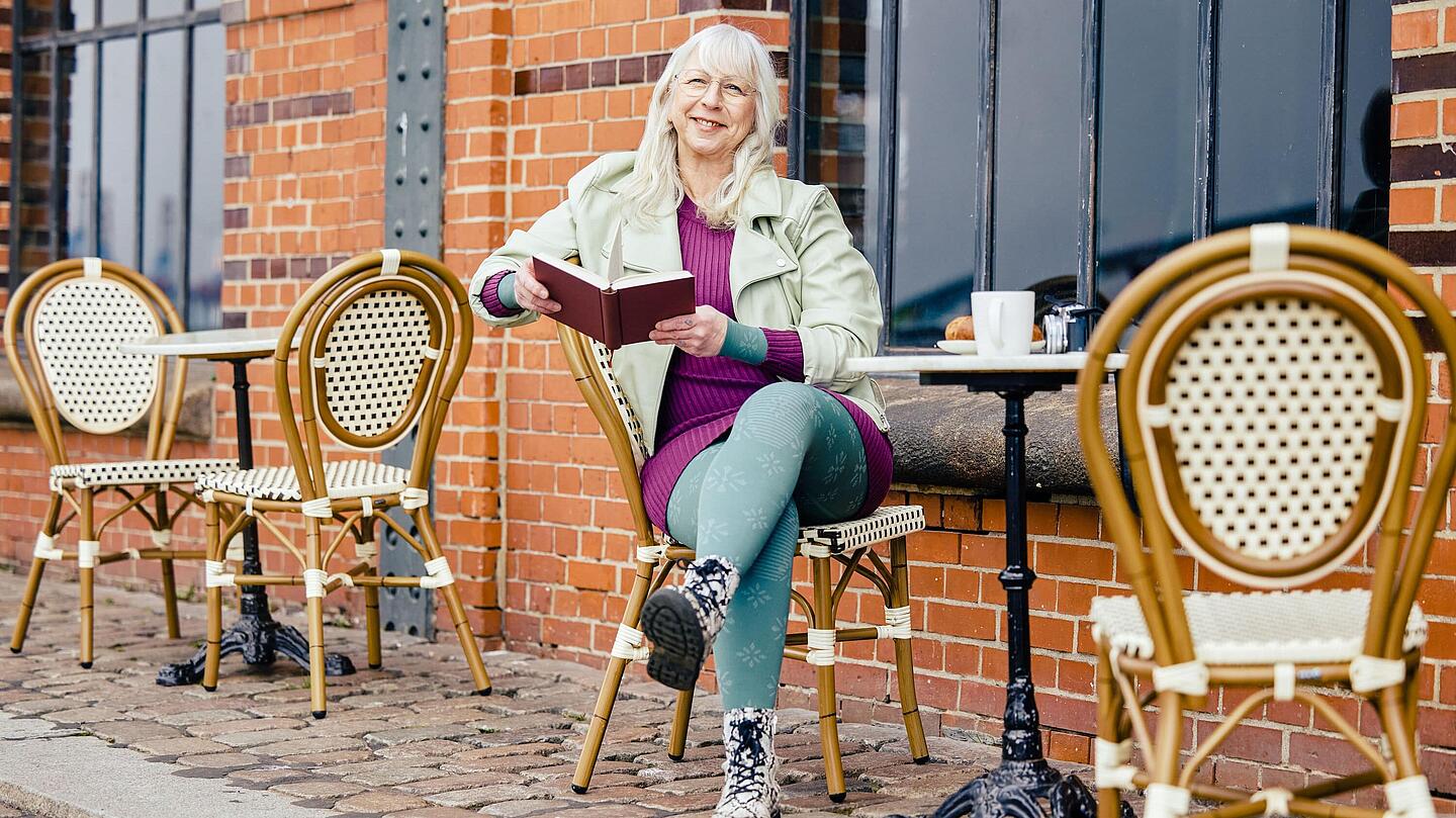 Frau mit Kompressionsstrumpfhosen sitzt mit einem Buch vor einem Café, Bildquelle: medi