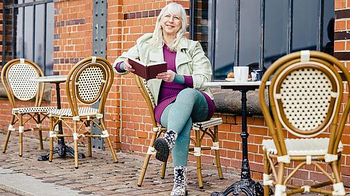 Frau mit Kompressionsstrumpfhosen sitzt mit einem Buch vor einem Café, Bildquelle: medi