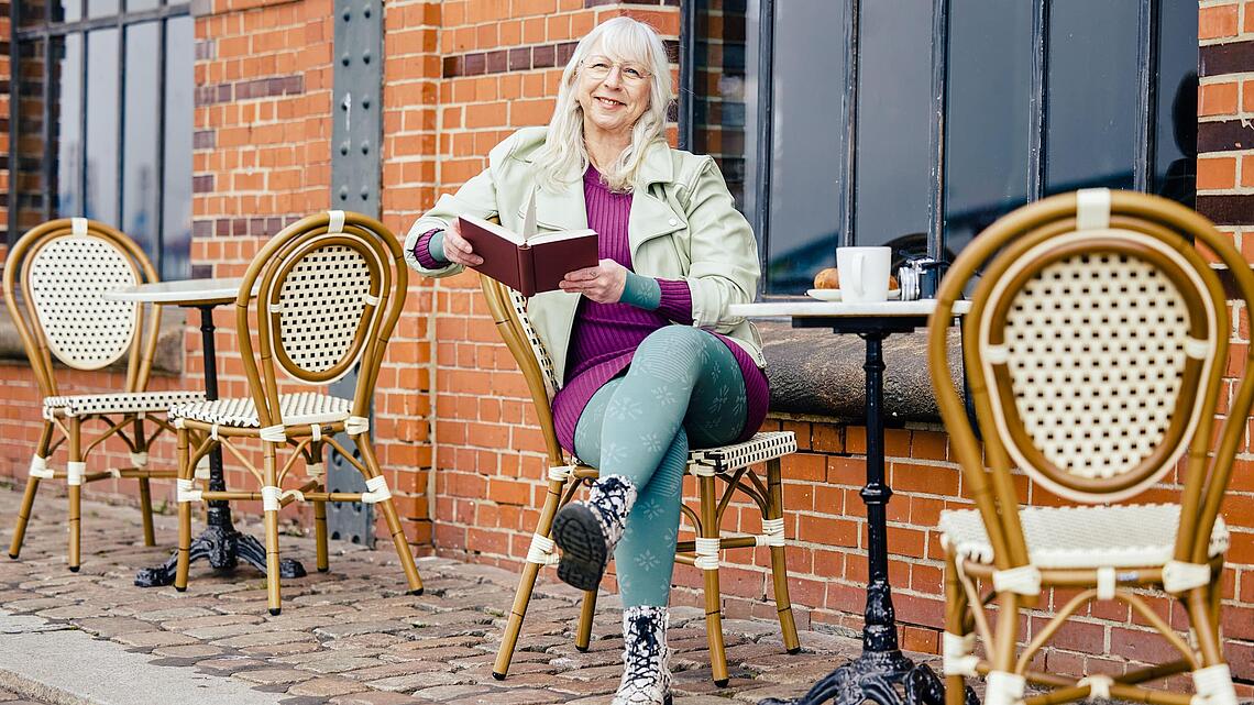 Frau mit Kompressionsstrumpfhosen sitzt mit einem Buch vor einem Café, Bildquelle: medi