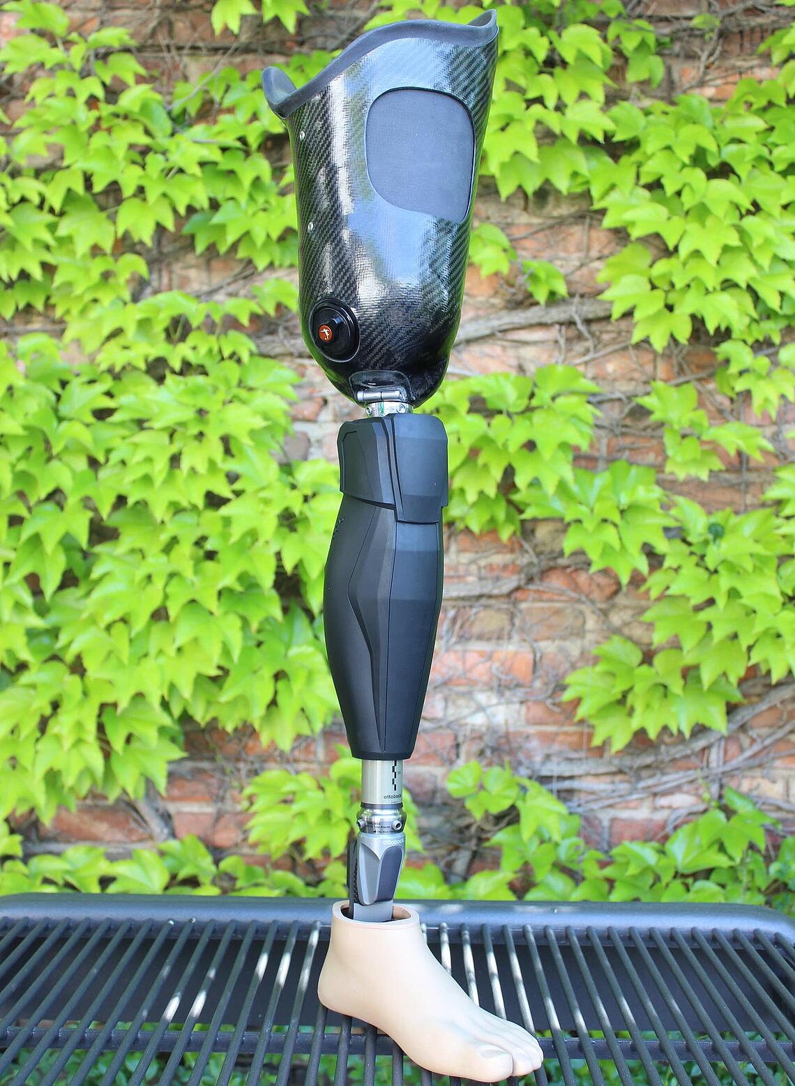 Oberschenkel-Prothese mit Genium-X3-Kniegelenk und Silikon-Innenschaft stehend vor efeubewachsener Mauer