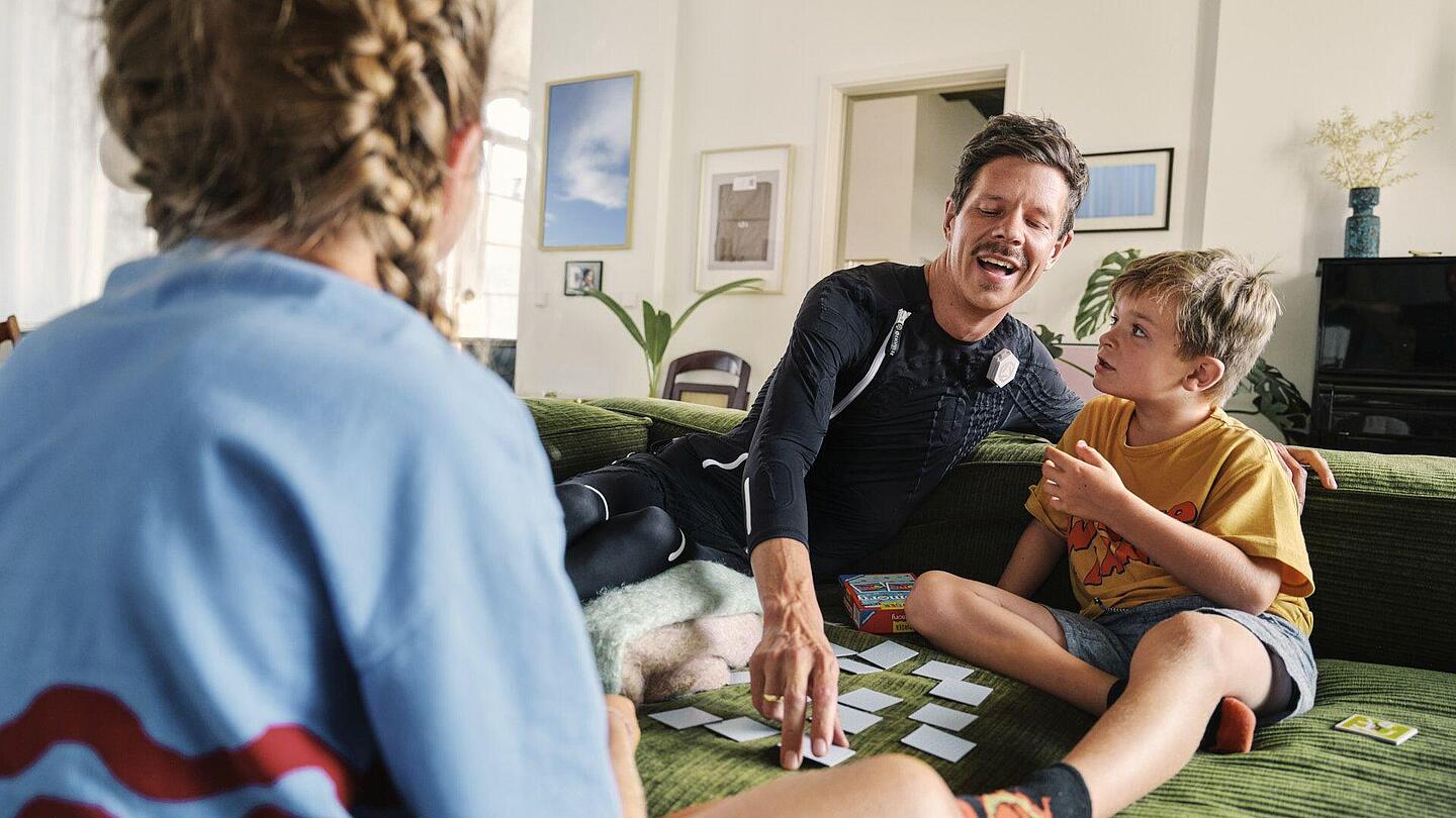 Mann im exopulse-suit-Anzug spielt auf der Couch Karten mit seinen Kindern, Quelle: ottobock
