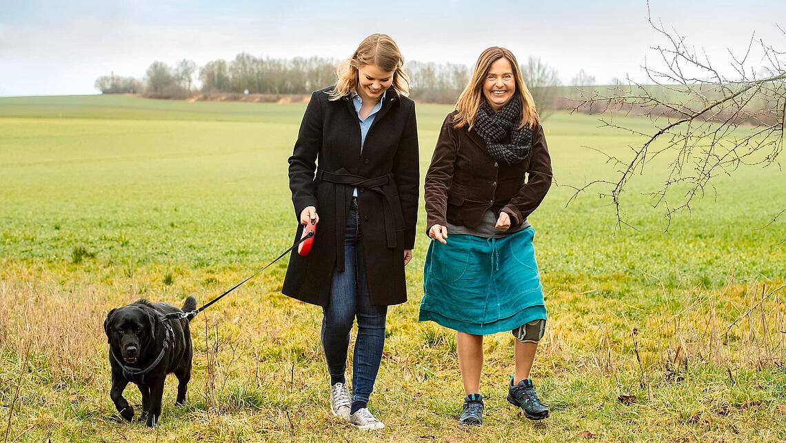 zwei Frauen die mit einem Hund über eine Wiese spazieren, eine trägt eine Knie-Manschette aufgrund einer Fußhebe-Schwäche, © Ottobock