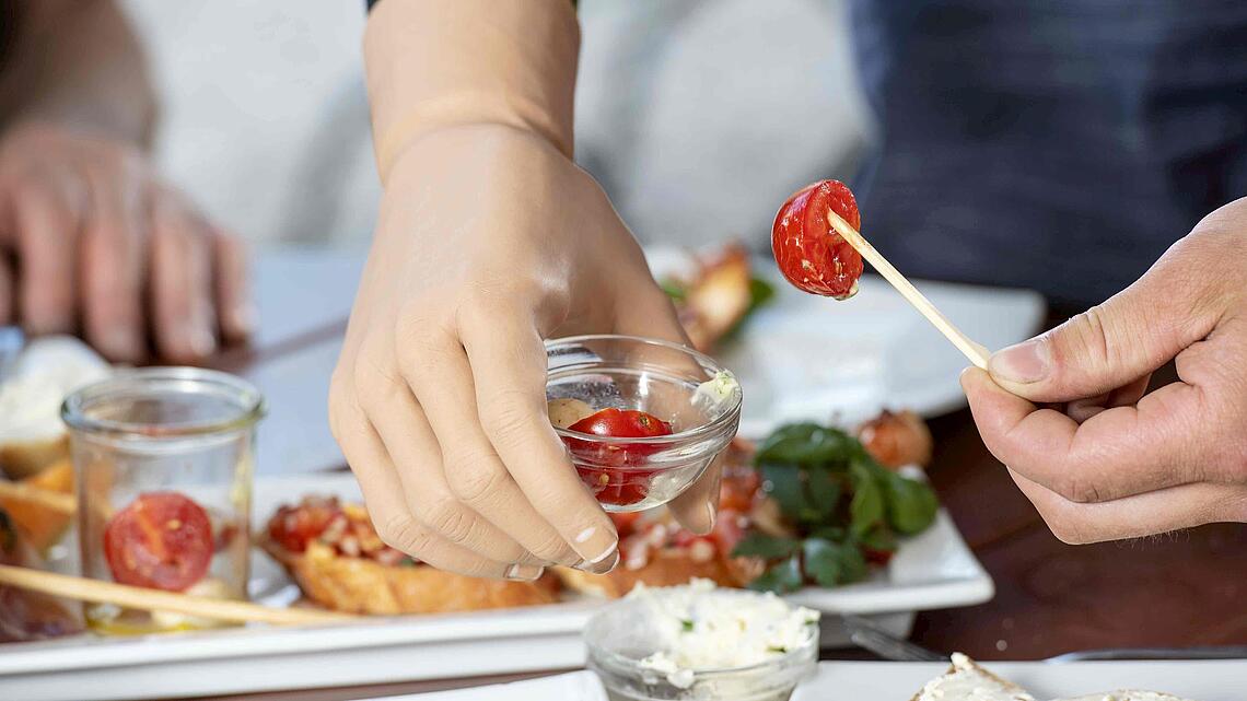 MyoPlus-Armprothese, die eine kleine Glasschale mit Essen am Buffet hält, © Ottobock
