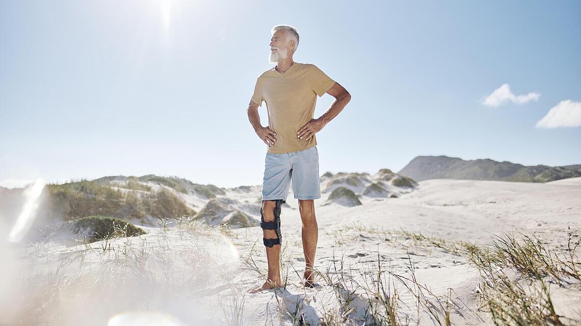 Mann am Strand mit Knie-Orthese, Quelle: Bauerfeind AG, Zeulenroda Mann steht am Strand und hat Orthese am Knie, Quelle: Bauerfeind AG, Zeulenroda