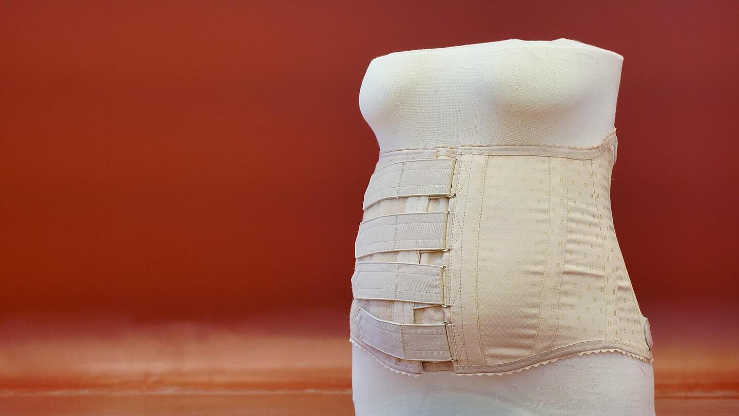 Vorderansicht eines Stützmieders nach Schanz  Vorderansicht eines Stützmieders nach Schanz mit vertikal verlaufenden Metallverstärkungsstäben vor rotem Hintergrund